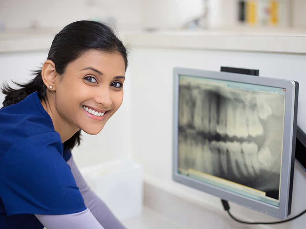 dental professional in scrubs viewing radiographs on computer monitor