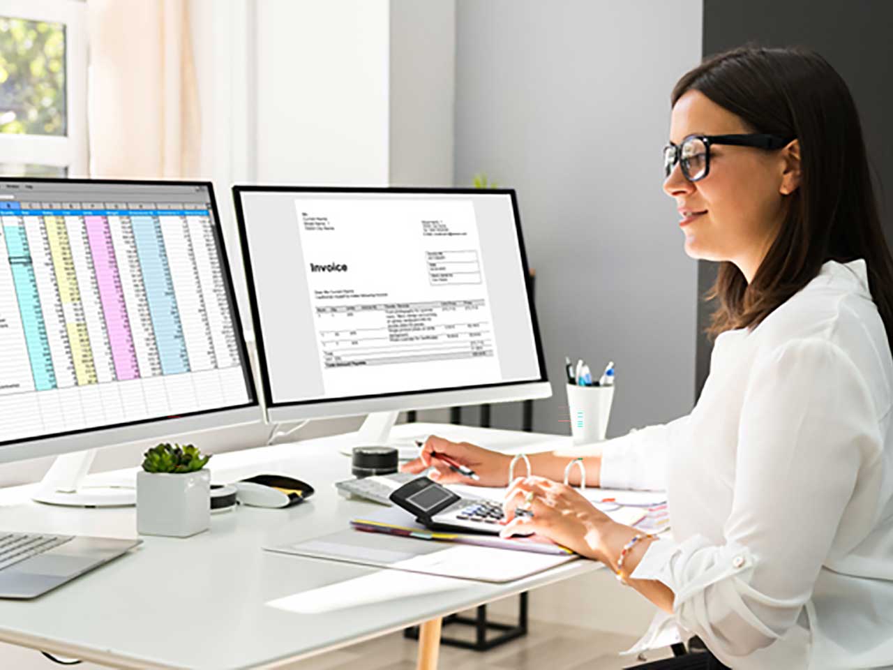 woman working at desk looking at financial charts on two computer monitors