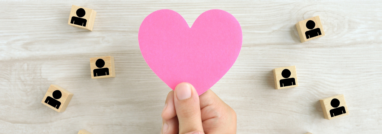 Hand holding a pink paper heart surrounded by wooden blocks with icons on them.