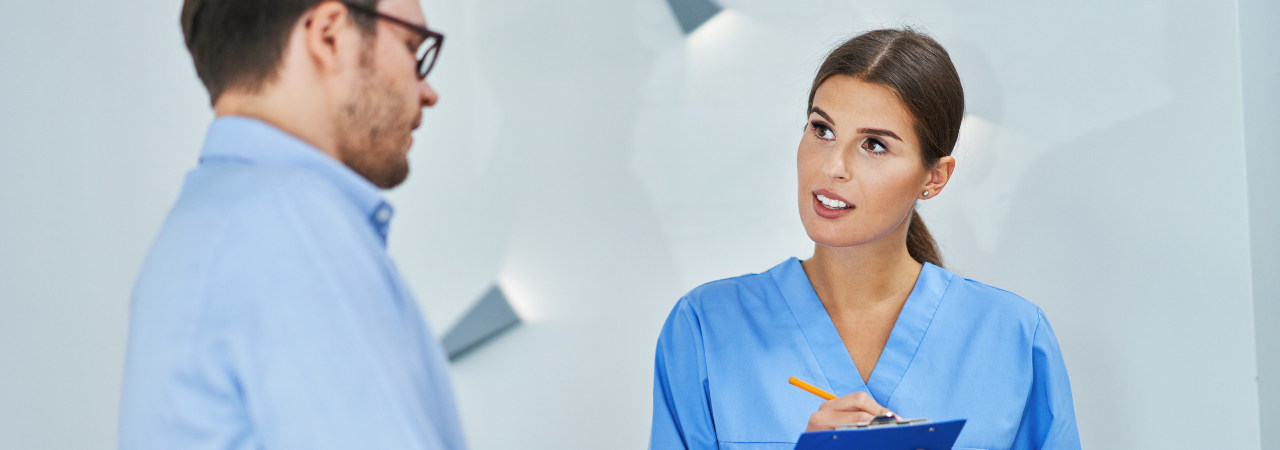 Dental assistant talking with a patient while taking notes on a clipboard