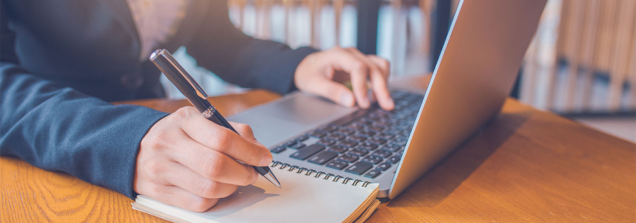 a person taking notes by a laptop