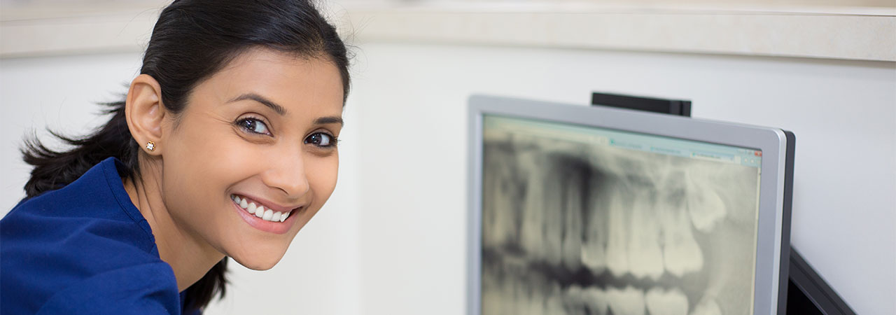 dental assistant smiling at camera with x-ray image on computer