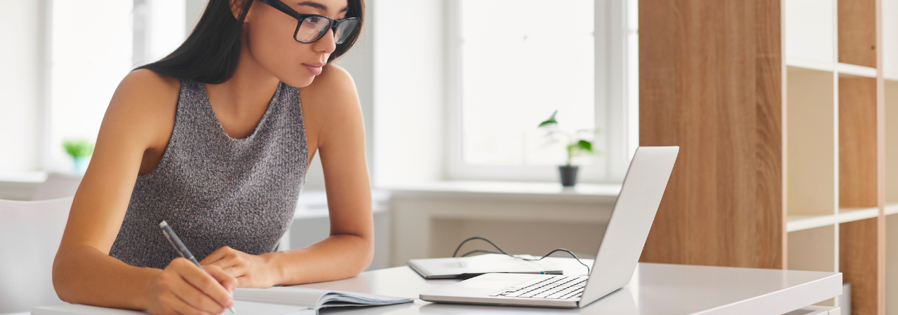 woman studying on laptop and writing down notes