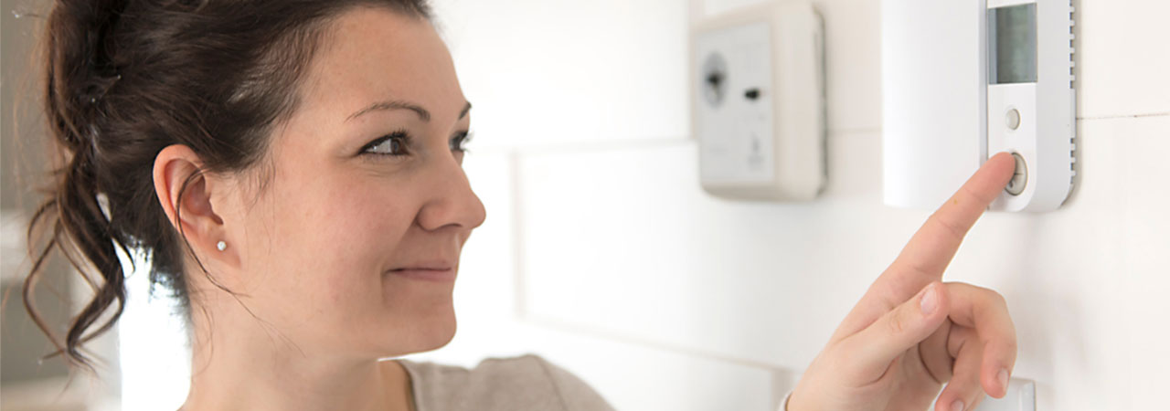 woman presses a button on a wall thermostat