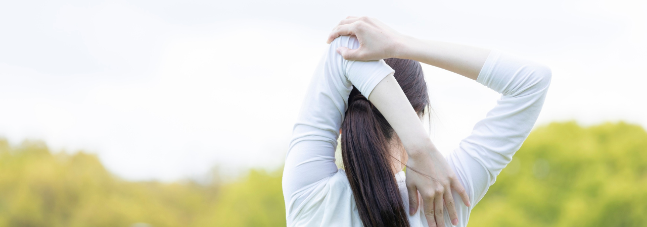 Person stretching their elbow behind their head in front of a green landscape