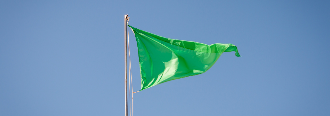 Green flag at the top of a flag pole against a blue sky