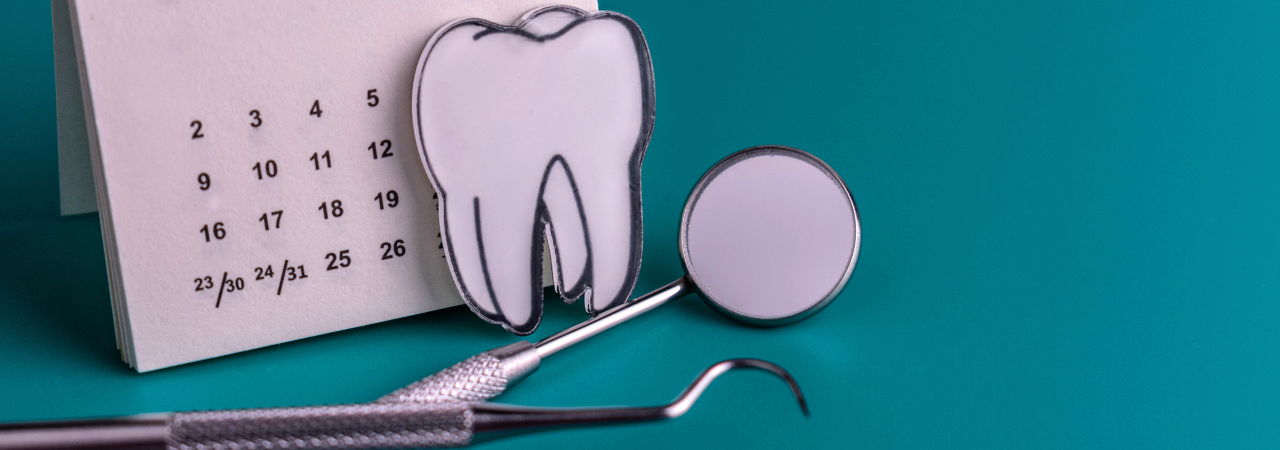Dental tools and a paper tooth in front of a small calendar against a turquoise background