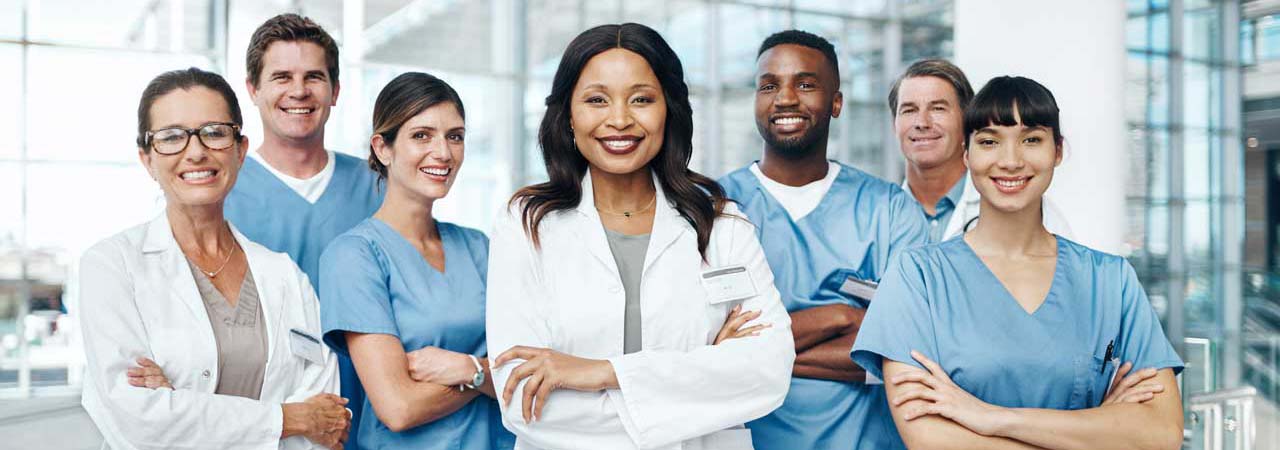 Group of dental health professionals in scrubs and white coates standing with arms crossed