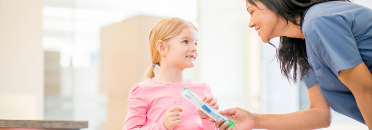 pediatric dental assistant hands a toothbrush to a child