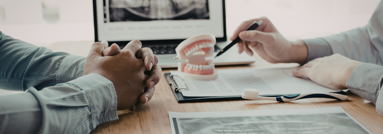 Two people discussing dental treatment options at a desk with xrays and a mouth model