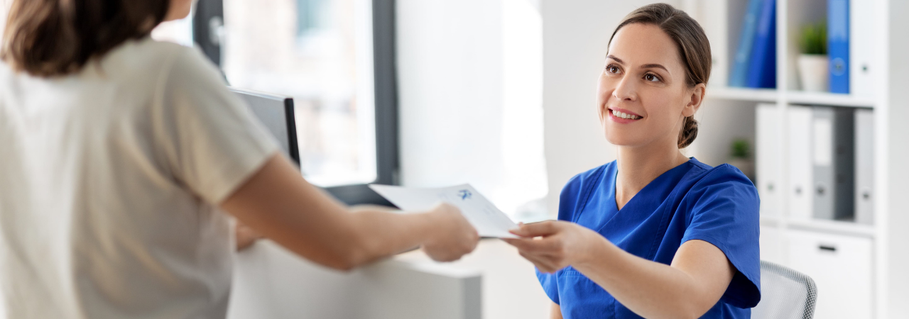 A dental assistant sitting behind a desk handing a patient paperwork