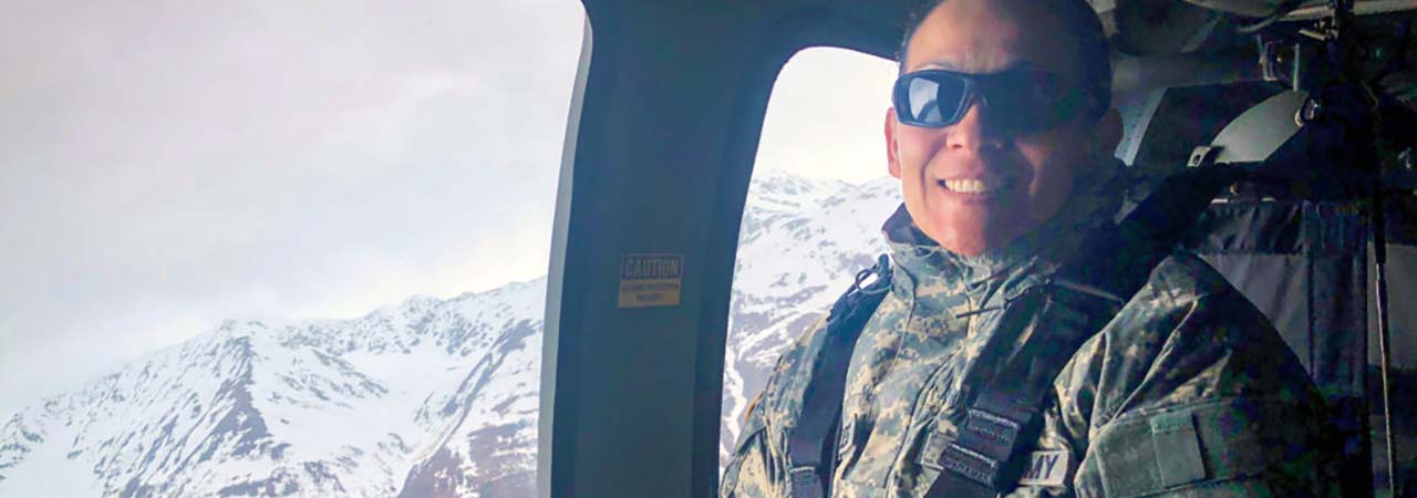 army member in helicopter with mountains in background