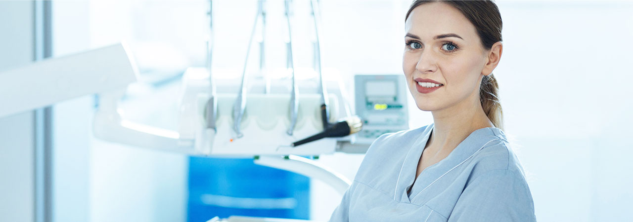 Dental assistant in scrubs in brightly lit dental exam room