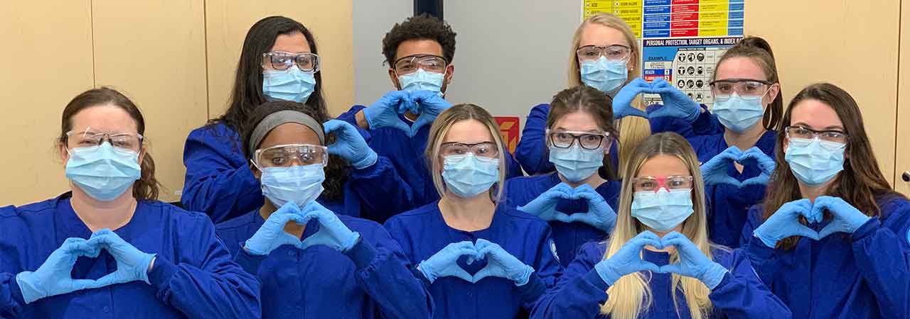 Dental assistants wearing masks and gloves making hearts with hands